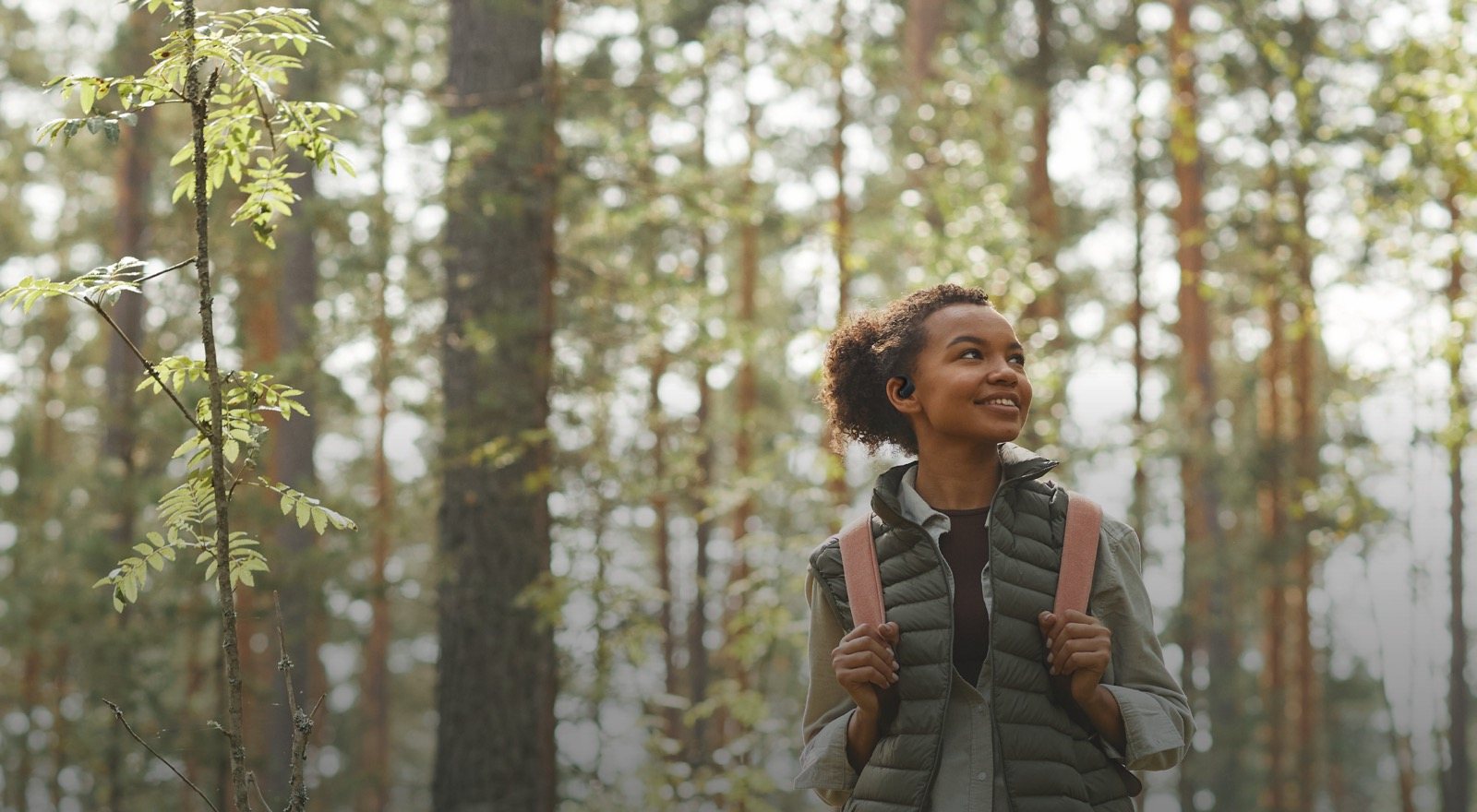 Vrouw luistert in het bos met REBØNE open-ear koptelefoon